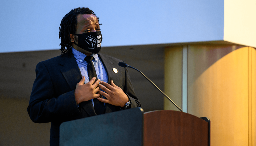 Masked man speaks at podium