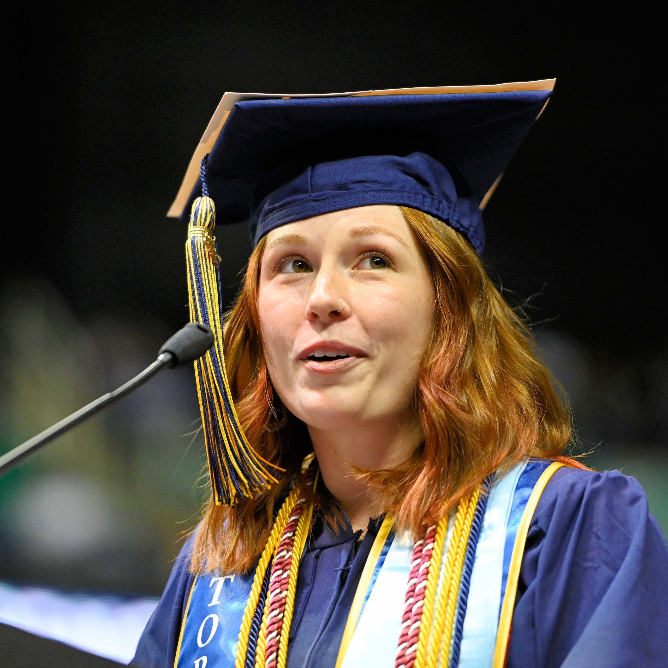 red haired girl in cap and gown speaks at podium