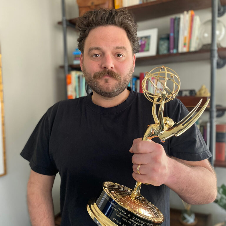 man with facial hair holds an emmy award statue