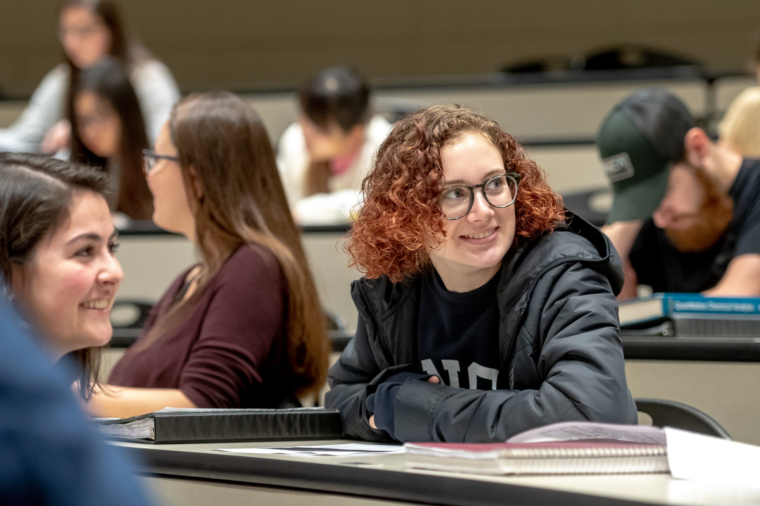 A woman is seated and smiling in a lecture hall