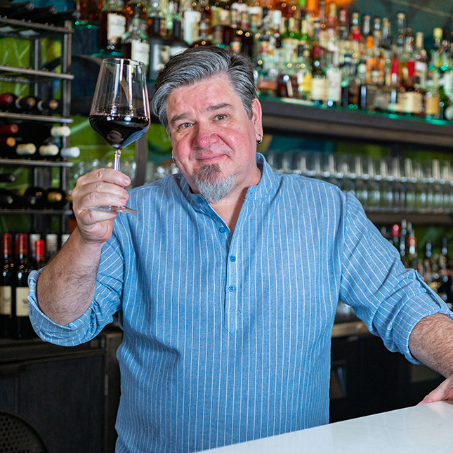 man with gray hair holds up glass of red wine