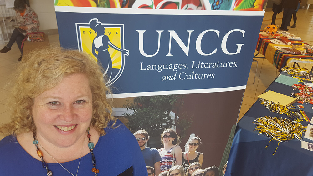 Amy Williamsen standing in front of a sign that reads UNCG Languages, Literatures, and Cultures