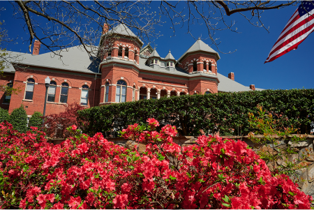 hot pink blooming azaleas in the foreground with the brick Foust building in the background and a clear blue sky.