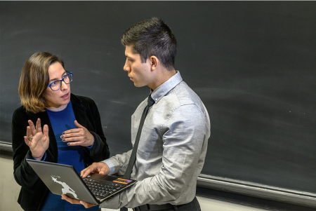 two people engaged in conversation in front of a blackboard.