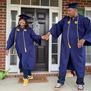 a man and woman walk and hold hands while dressed in caps and gowns with honors cords.