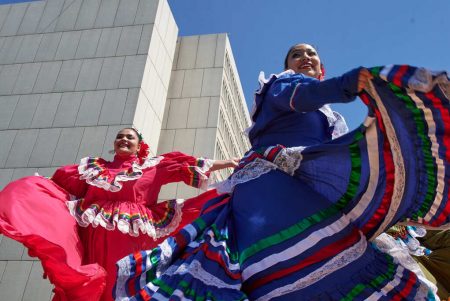 two women wearing colorful mexican dresses, flaunting and dancing