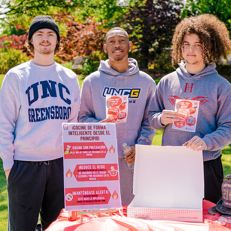 Three male UNCG students hold up fire safety signs