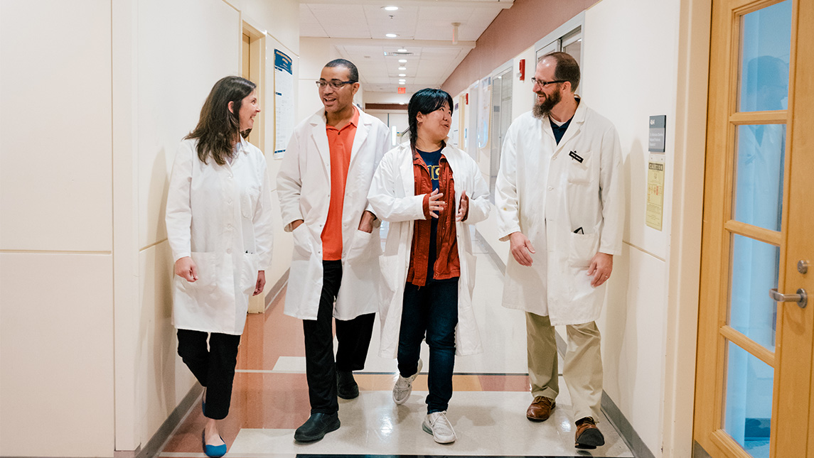 four people in lab coats walking down a hall together in conversation