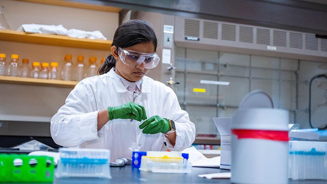 a young woman in a lab coat wearing googles and gloves while handling lab equipment