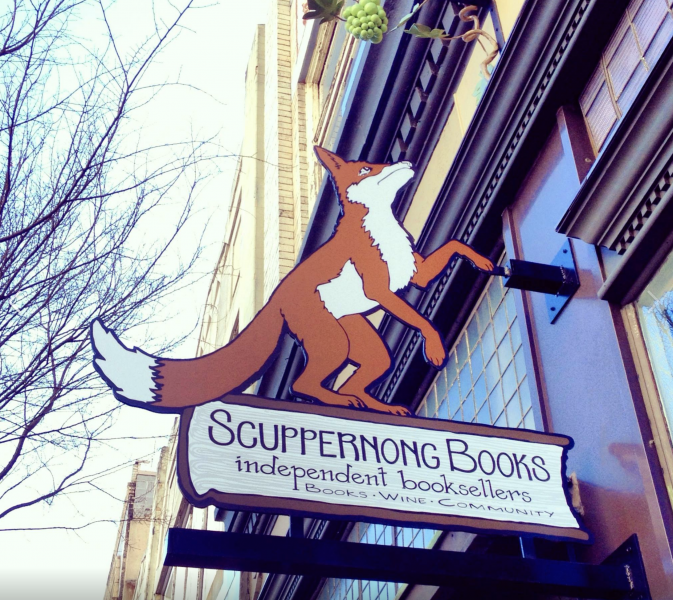 the outside of Scuppernong Books with their sign up on the wall, featuring a fox that looks like it's about to climb the building.