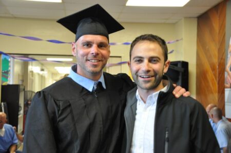 Inmate wearing graduation cap and gown, poses with Professor Kaplan