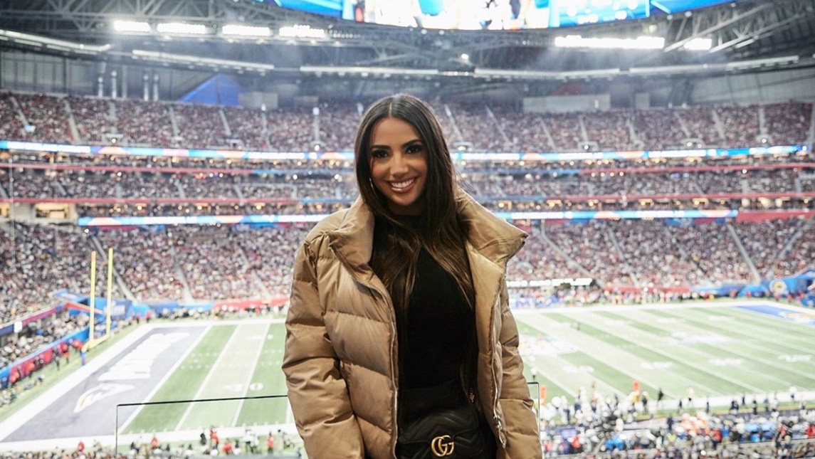 Dominique stands in coat in front of super bowl football field