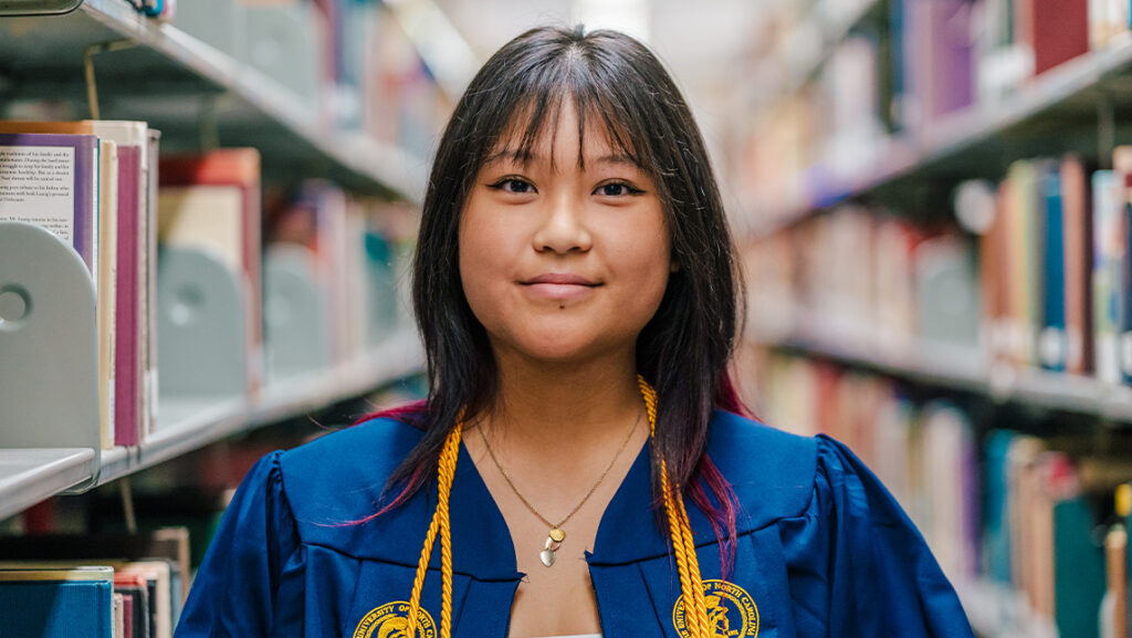 Tiffany Tan in graduate robe in front of rows of books