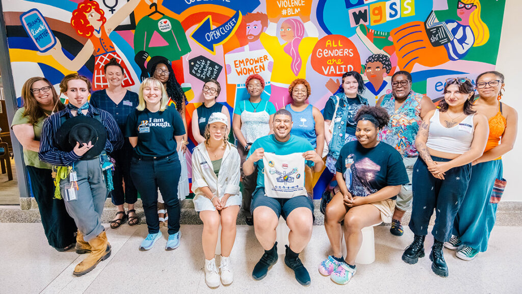 A group of students stands in front of a colorful mural in the WGSS department.