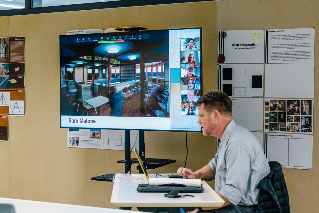 interior architecture instructor seated in front of a screen showing a rendering of a room design.