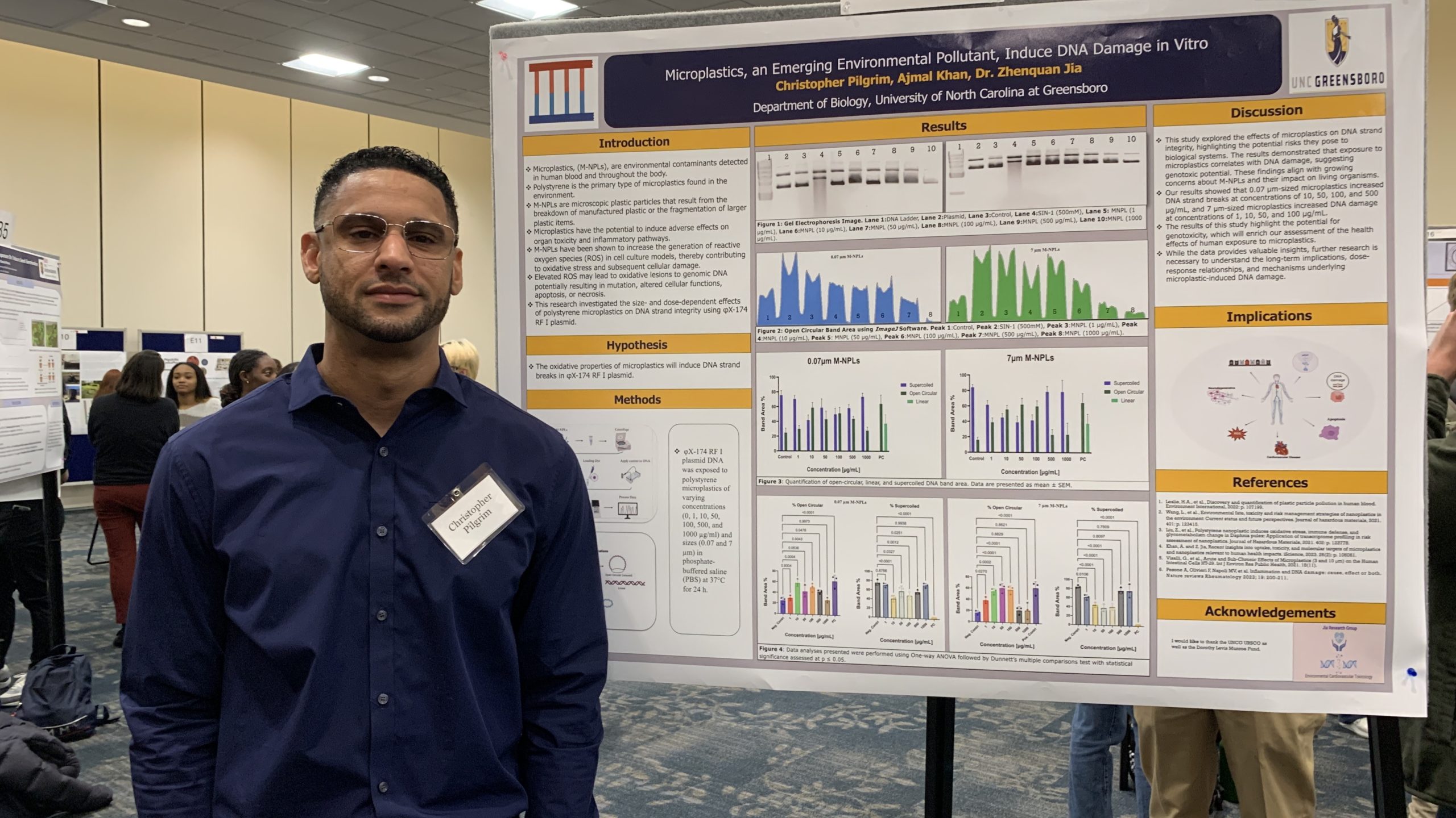 Picture of Christopher Pilgrim standing in front of a poster presenting scientific research.