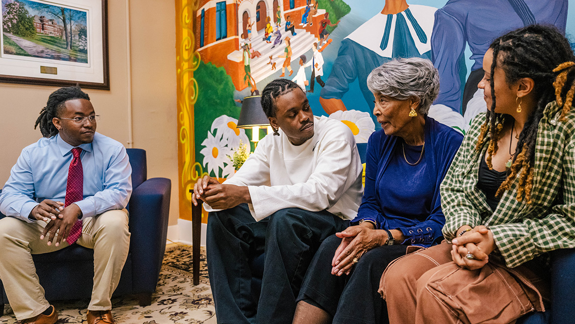 Mural artists sit with Joanne Smart Drane in front of mural