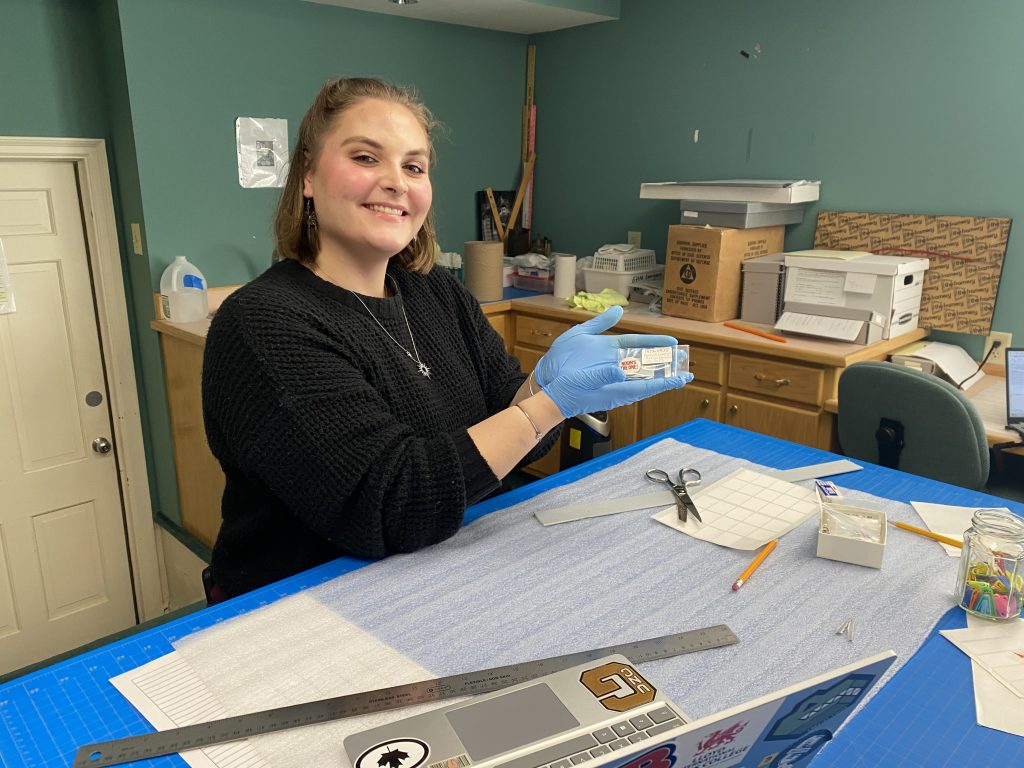 Student wearing gloves holds up historical pin. 