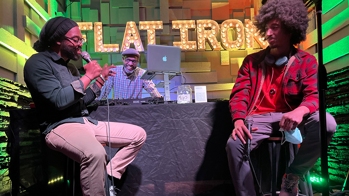 two men talk with microphones while DJ smiles and looks on