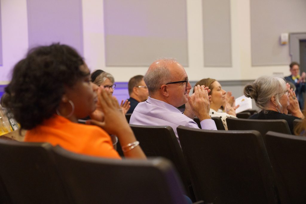A group of ceremony attendees applaud for the Humanities at Work class.