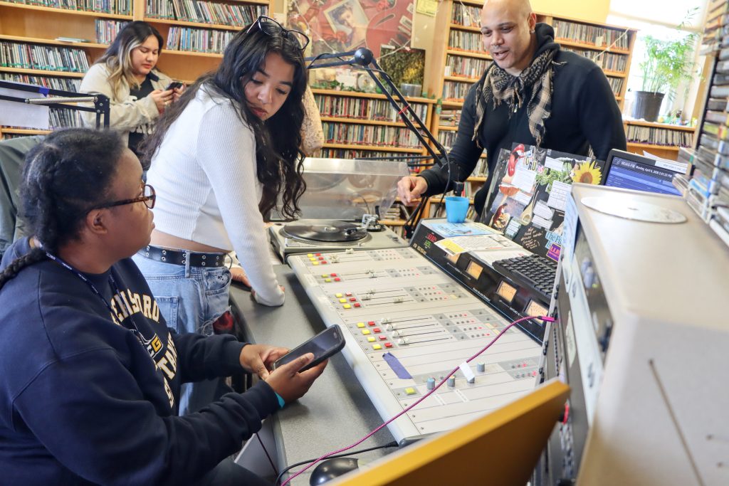 Students and an instructor gather around the WUAG radio station control board as they learn radio broadcasting and studio operations.