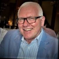 A closeup photo of a man--Vince Henrich--in glasses and wearing a suitcoat smiling at the camera. 