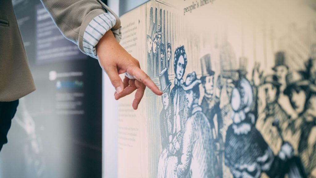 a person pointing to an illustration of historical people in an exhibit.